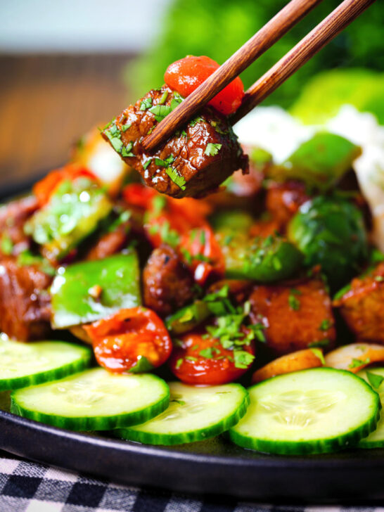 Vietnamese shaking beef (bò lúc lắc) served with cucumber, rice and lettuce being picked up with chopsticks.