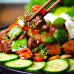 Vietnamese shaking beef (bò lúc lắc) served with cucumber, rice and lettuce being picked up with chopsticks.