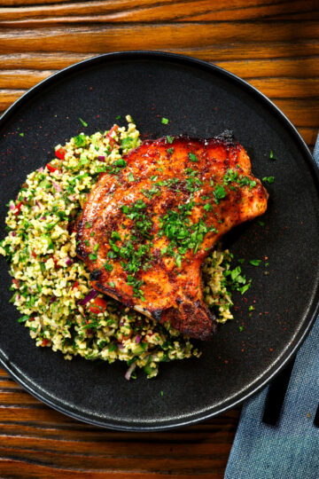 Overhead baked harissa and honey glazed pork chops served with parsley and tabbouleh.
