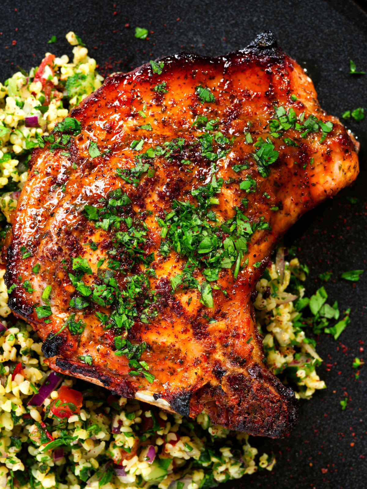 Close-up overhead baked harissa and honey glazed pork chops served with parsley and tabbouleh.