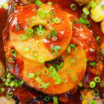 Close-up overhead baked Hawaiian chicken breast with pineapple huli huli sauce and crushed new potatoes.