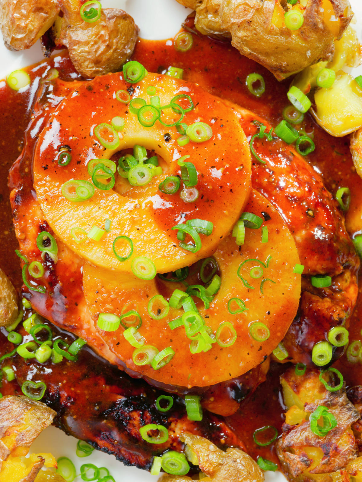 Close-up overhead baked Hawaiian chicken breast with pineapple huli huli sauce and crushed new potatoes.