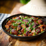 Harissa beef tagine with prunes and almonds in a traditional style pot garnished with coriander.