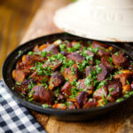 Overhead harissa beef tagine with prunes and almonds in a traditional style pot.