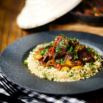 Overhead harissa beef tagine with prunes and almonds served with buttered couscous.