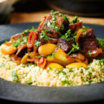 Close-up harissa beef tagine with prunes and almonds served with buttered couscous.