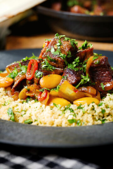 Close-up harissa beef tagine with prunes and almonds served with buttered couscous.