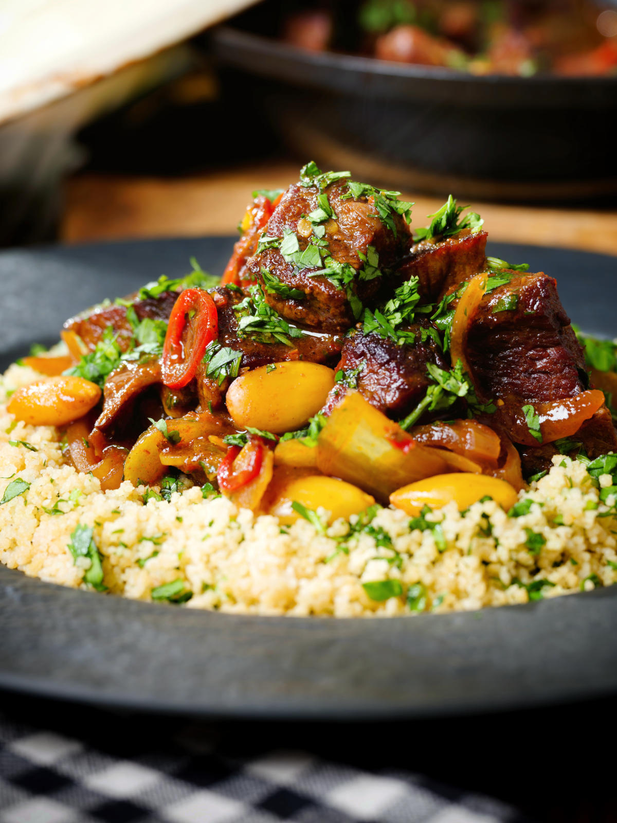 Close-up harissa beef tagine with prunes and almonds served with buttered couscous.