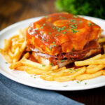 Portuguese francesinha sandwich served with a beer sauce and French fries.