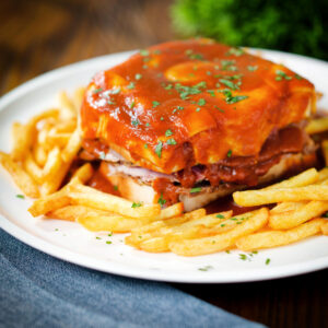 Portuguese francesinha sandwich served with a beer sauce and French fries.