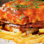 Close-up Portuguese francesinha sandwich served with a beer sauce and crispy French fries.