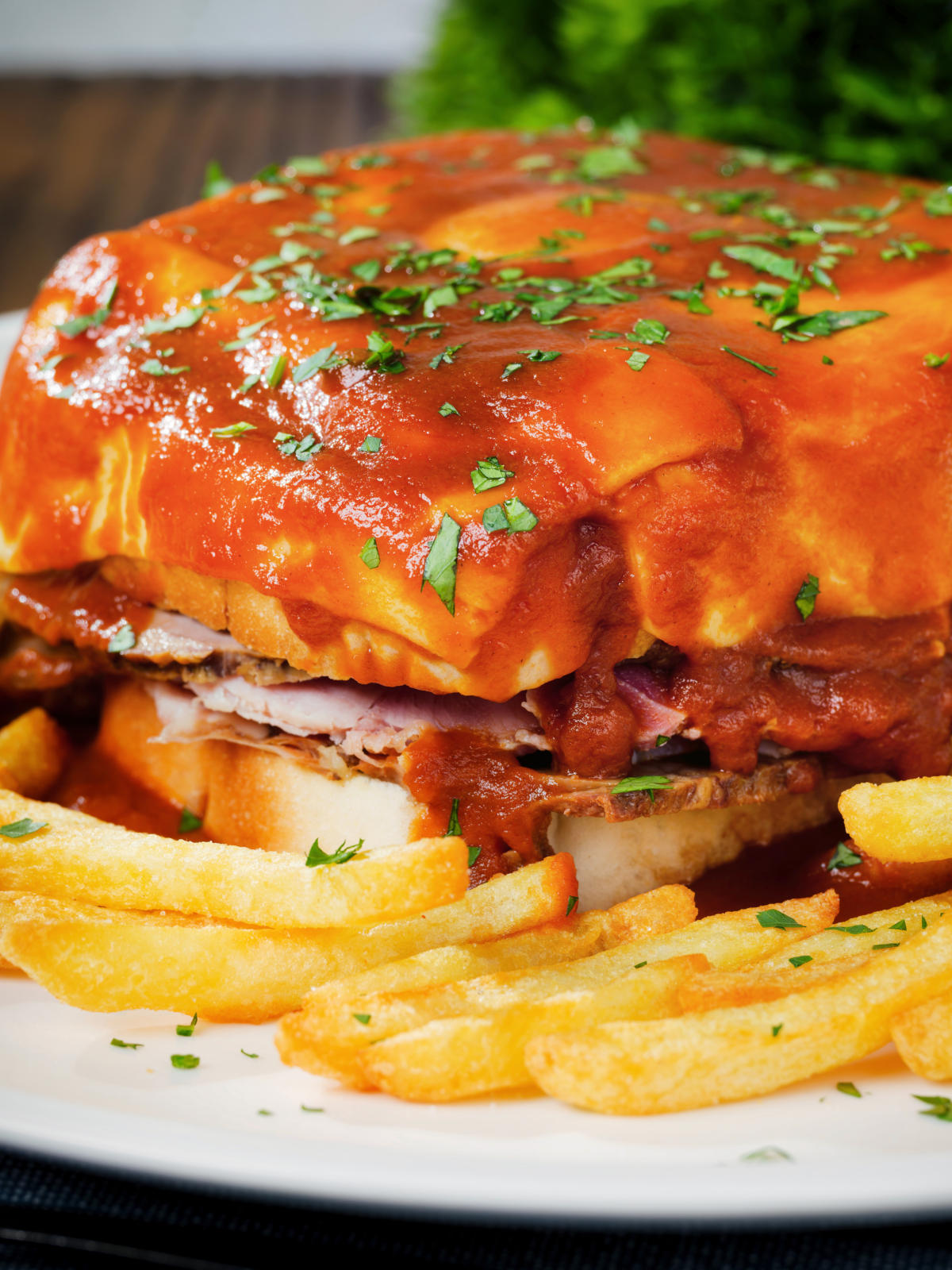 Close-up Portuguese francesinha sandwich served with a beer sauce and crispy French fries.