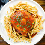 Overhead Portuguese francesinha sandwich served with a beer sauce and French fries.