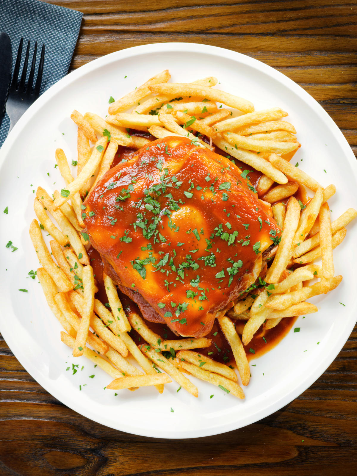 Overhead Portuguese francesinha sandwich served with a beer sauce and French fries.