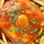 Close-up overhead Portuguese francesinha sandwich served with a beer sauce and French fries.