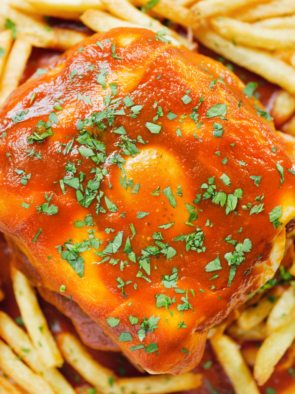 Close-up overhead Portuguese francesinha sandwich served with a beer sauce and French fries.
