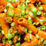 Close-up overhead spicy gochujang sausage pasta garnished with spring onions.