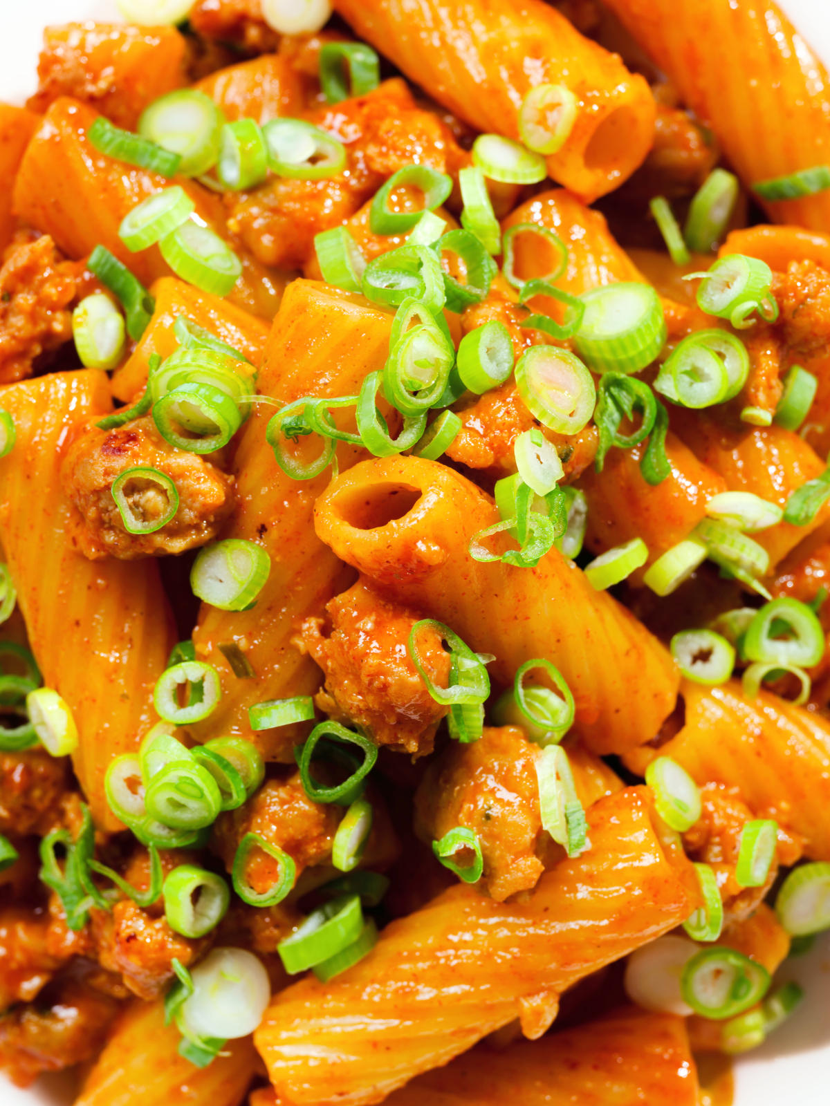 Close-up overhead spicy gochujang sausage pasta garnished with spring onions.
