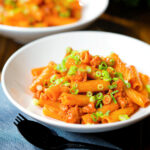 Spicy gochujang sausage pasta garnished with spring onions.