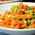 Close-up spicy gochujang sausage pasta garnished with spring onions.