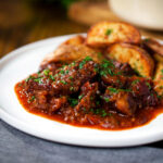 Greek beef kapama stew served with potato wedges and parsley.