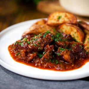 Greek beef kapama stew served with potato wedges and parsley.