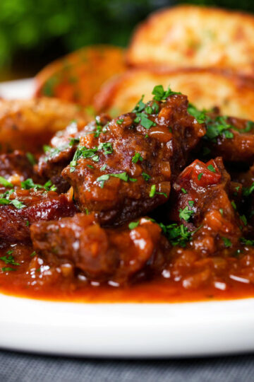 Close-up Greek beef kapama stew served with potato wedges.