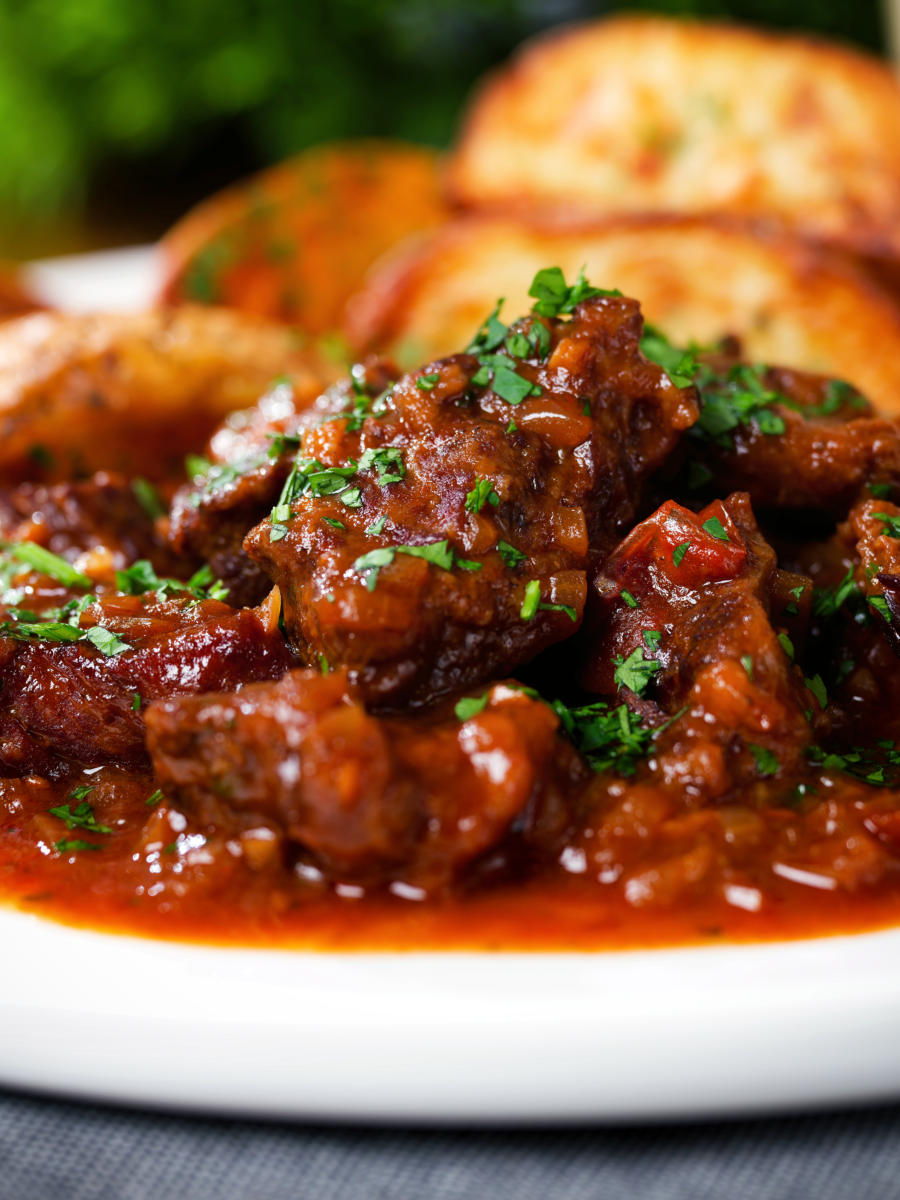 Close-up Greek beef kapama stew served with potato wedges.