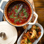 Overhead Greek beef kapama stew in its cooking pot served with potato wedges.