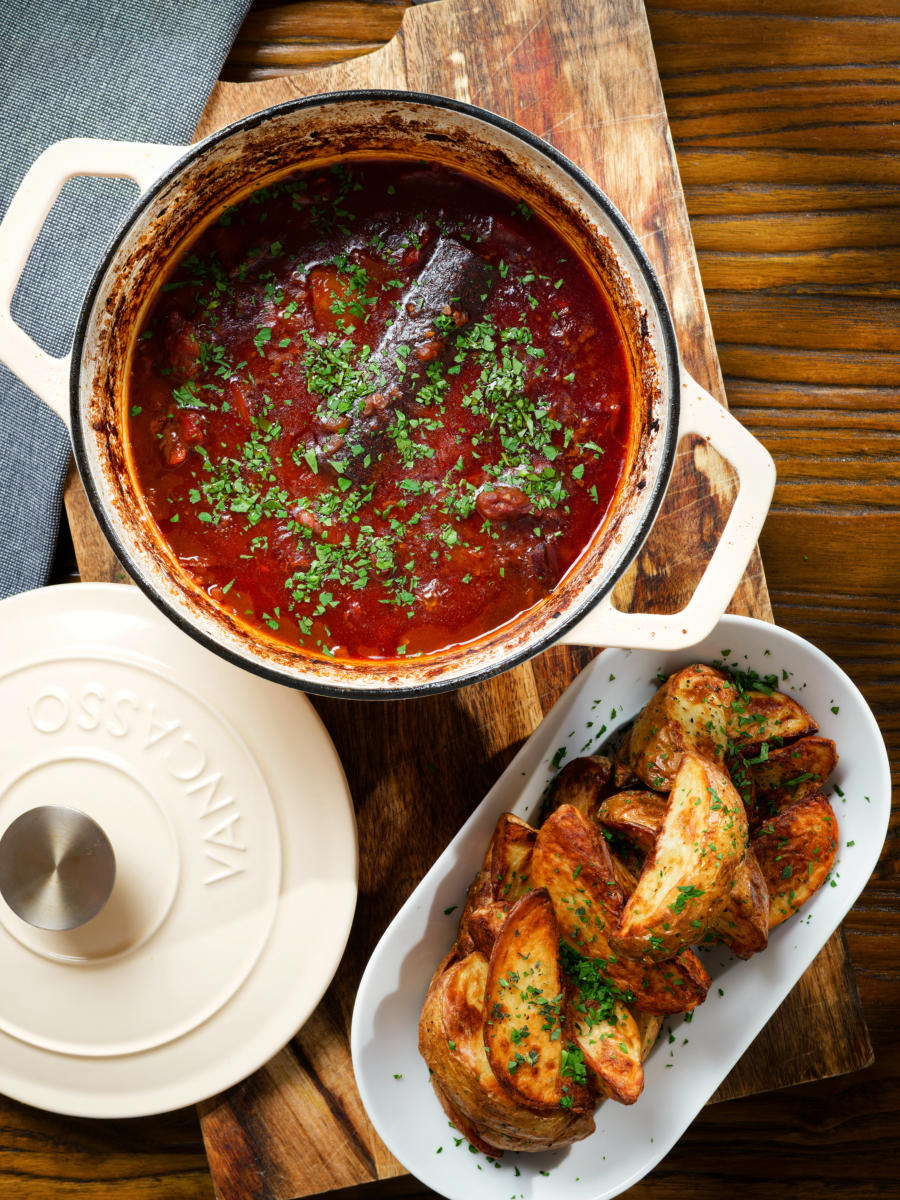 Overhead Greek beef kapama stew in its cooking pot served with potato wedges.