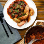 Overhead Greek beef kapama stew served with potato wedges.