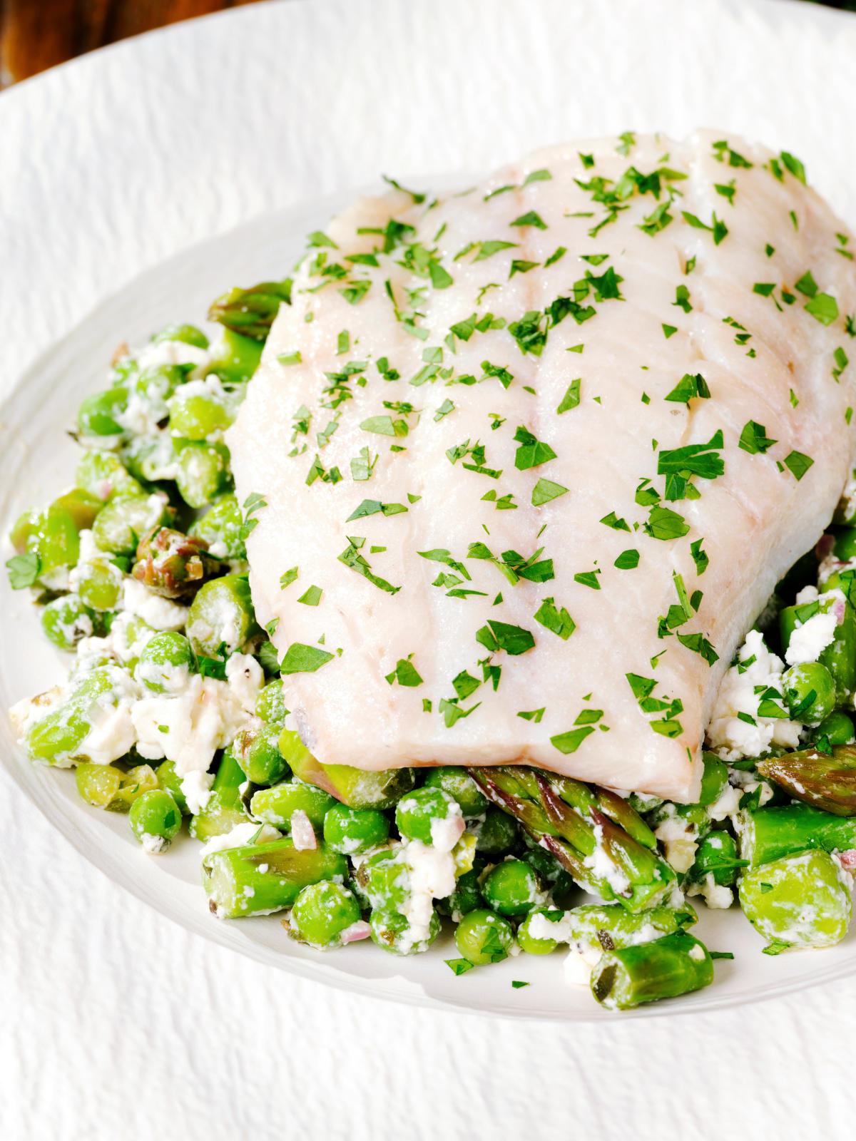 Close-up milk poached smoked haddock served with warm pea and feta salad.