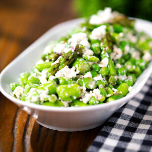 Minted pea and feta salad with asparagus and broad beans served in a white bowl.