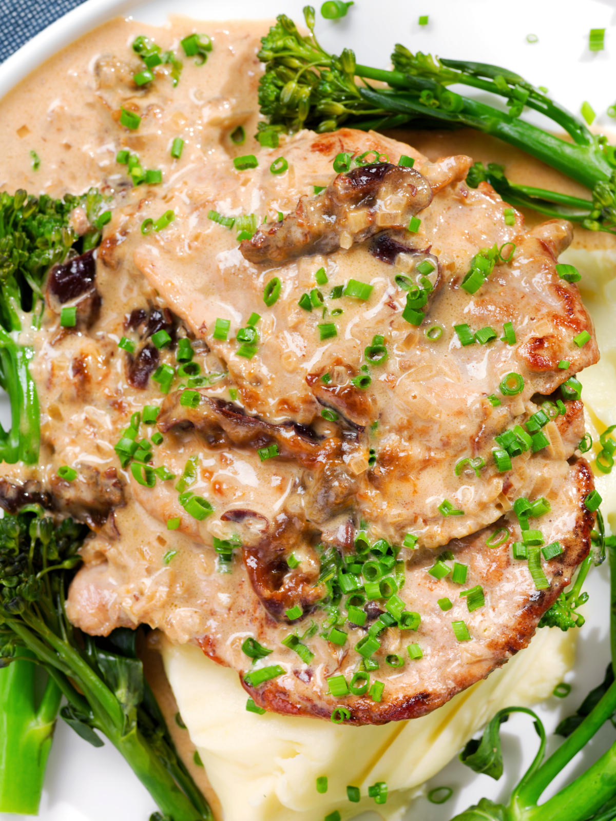 Close-up overhead pork tenderloin with prunes and brandy cream sauce, mashed potato and tenderstem broccoli.