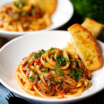 Tomato and mushroom pasta garnished with parsley served with garlic bread.