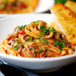 Close-up tomato and mushroom pasta garnished with parsley served with garlic bread.