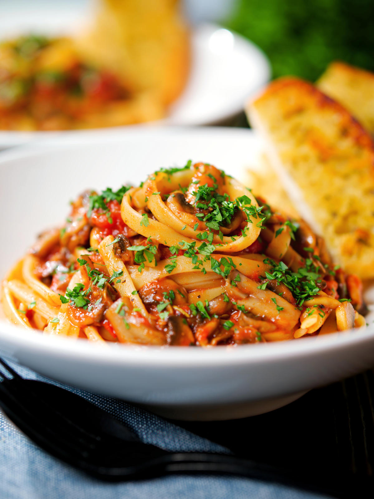 Close-up tomato and mushroom pasta garnished with parsley served with garlic bread.