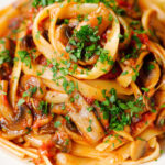 Close-up tomato and mushroom pasta garnished with parsley.