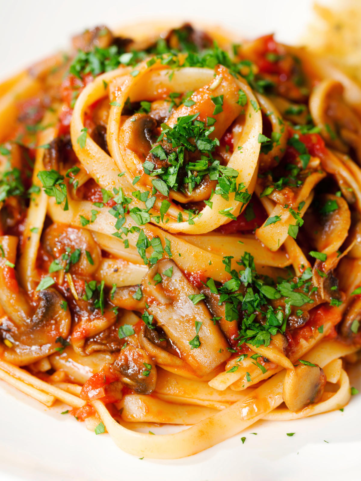 Close-up tomato and mushroom pasta garnished with parsley.