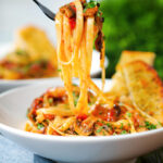 Tomato and mushroom pasta on a fork served with garlic bread.