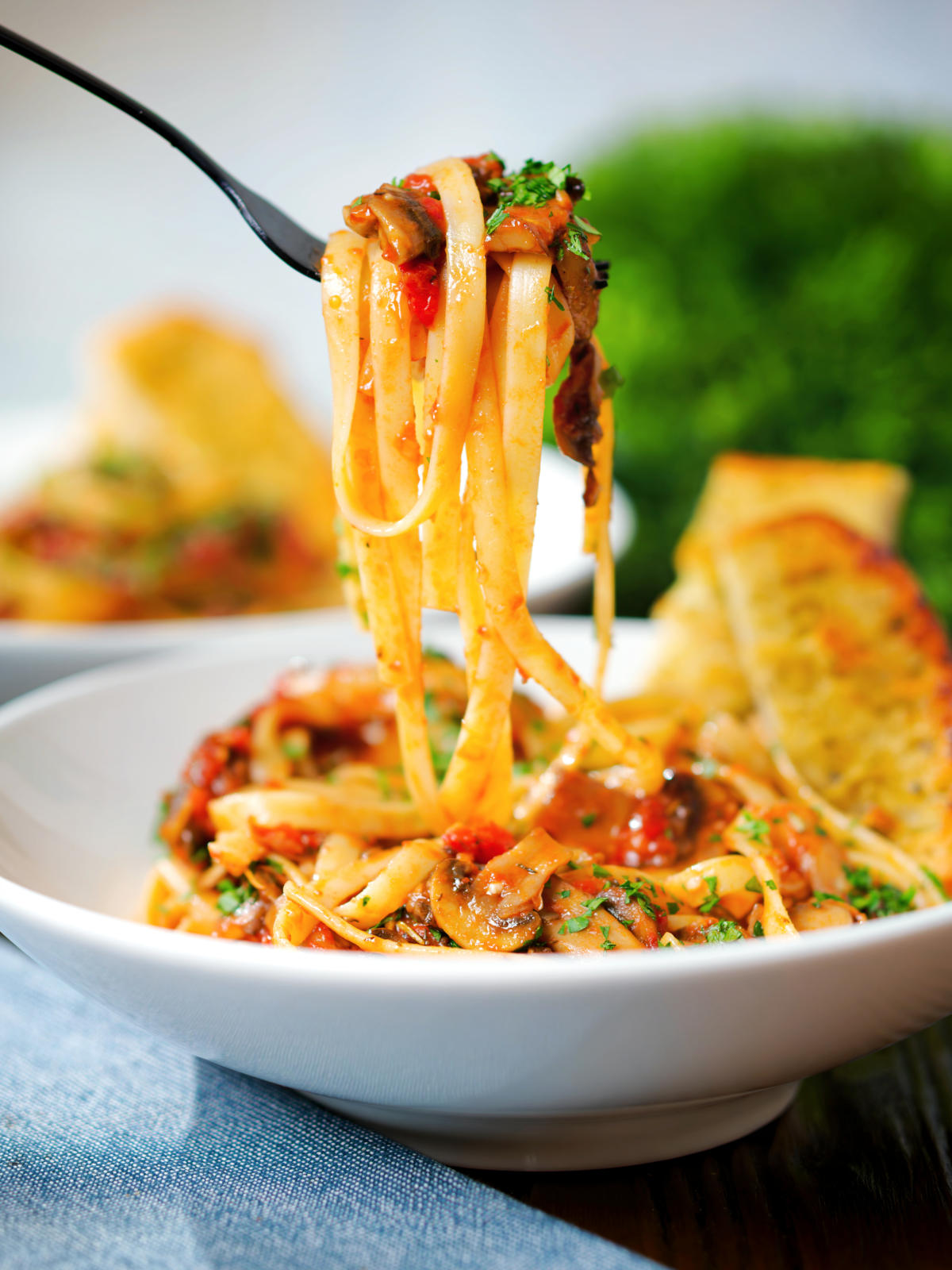 Tomato and mushroom pasta on a fork served with garlic bread.
