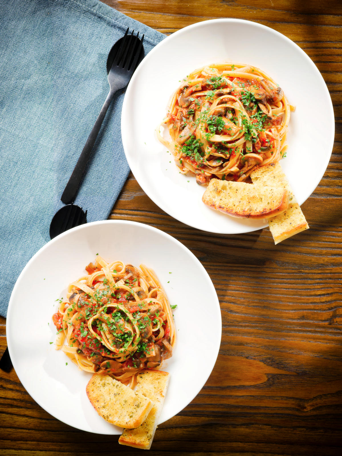 Overhead tomato and mushroom pasta on a fork served with garlic bread.