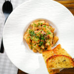 Overhead tinned tuna tomato pasta with capers, served with garlic bread.