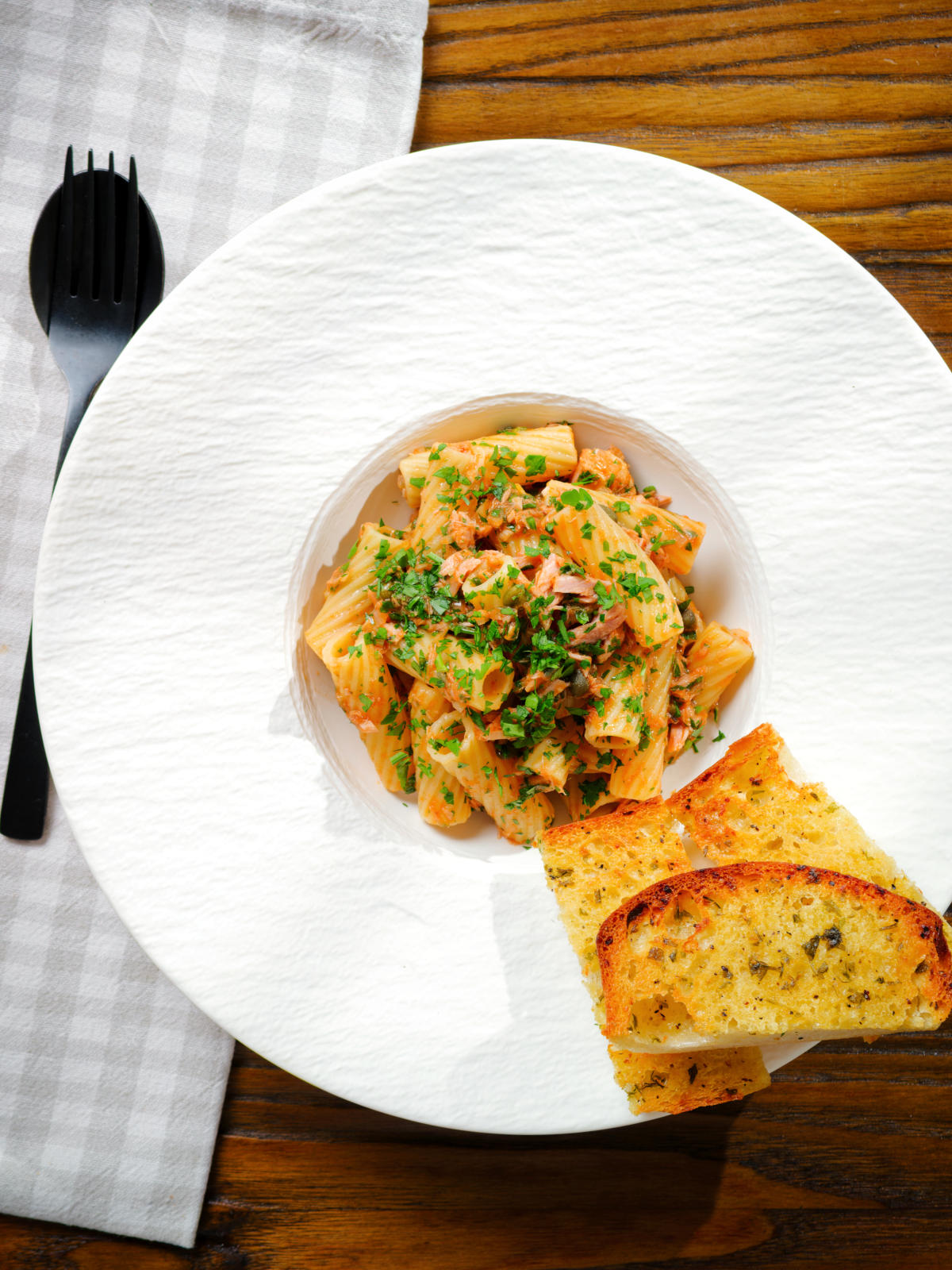 Overhead tinned tuna tomato pasta with capers, served with garlic bread.