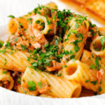 Close-up tinned tuna tomato pasta with capers, served with garlic bread.
