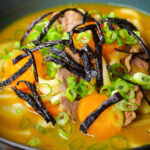 Close-up Japanese curry udon soup with beef and vegetables, nori and spring onions.