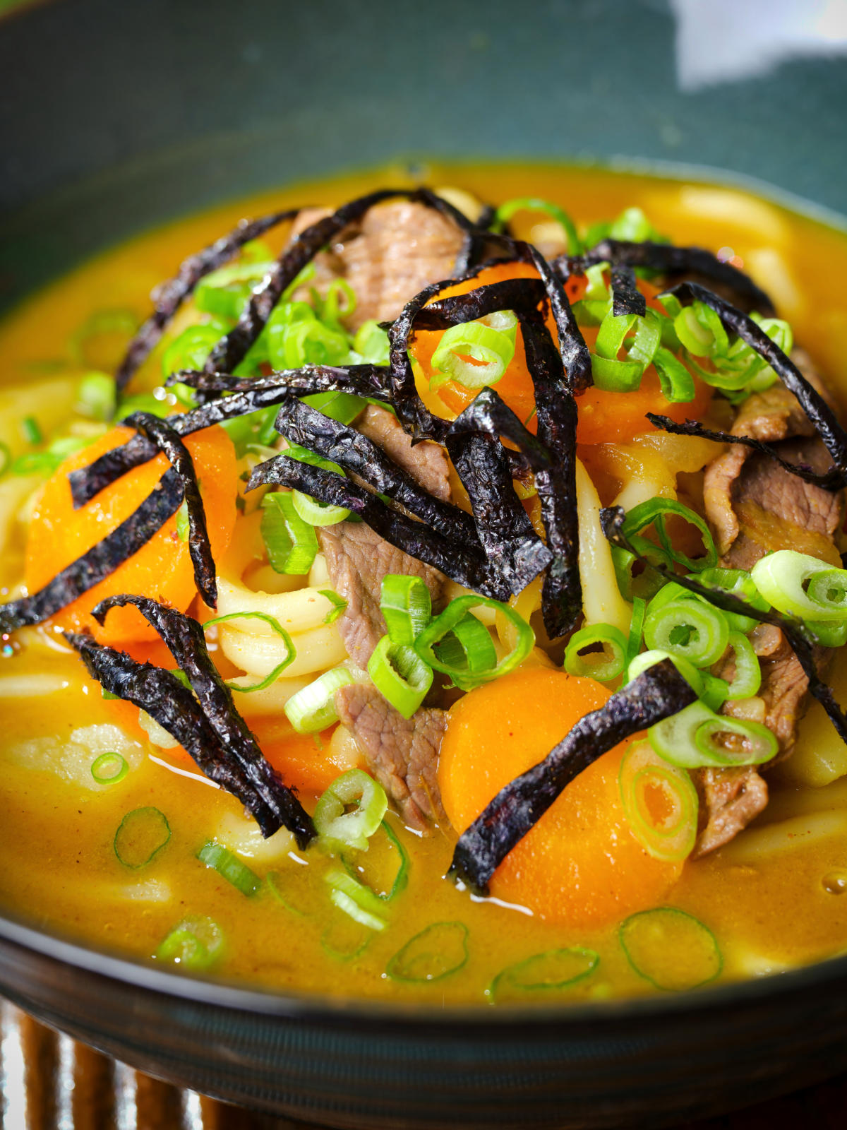 Close-up Japanese curry udon soup with beef and vegetables, nori and spring onions.