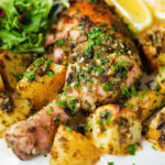Close-up Greek roasted chicken legs with potatoes, lemon and garlic served with a side salad.
