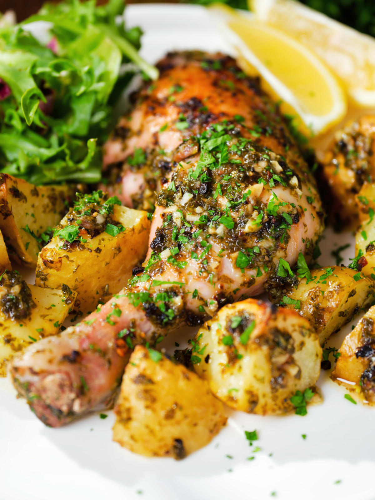 Close-up Greek roasted chicken legs with potatoes, lemon and garlic served with a side salad.