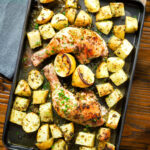 Overhead Greek roasted chicken legs with potatoes, lemon and garlic in a roasting tray.